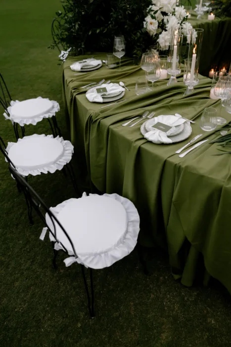 Wrought-iron chairs with ruffled white cushions pulled up to a table of soft green linen