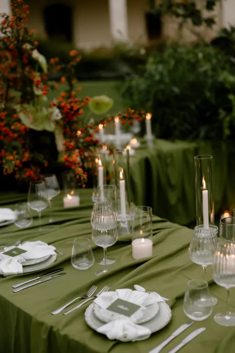Taper candles and ribbed glassware on a green table, with orange berry branches behind