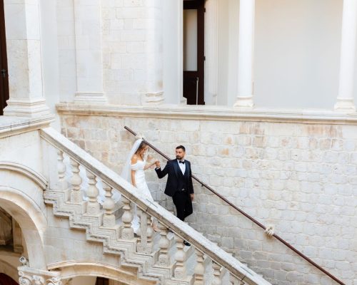 The bride and groom walk down a grand staircase together, the elegance of the moment captured by Kristijan Rezo.