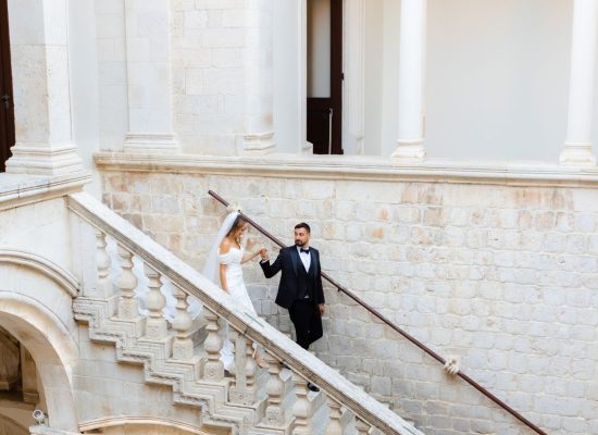 The bride and groom walk down a grand staircase together, the elegance of the moment captured by Kristijan Rezo.