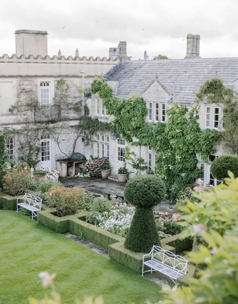 A view across the manicured gardens of Euridge Manor, with climbing vines and shaped topiary against the manor walls.