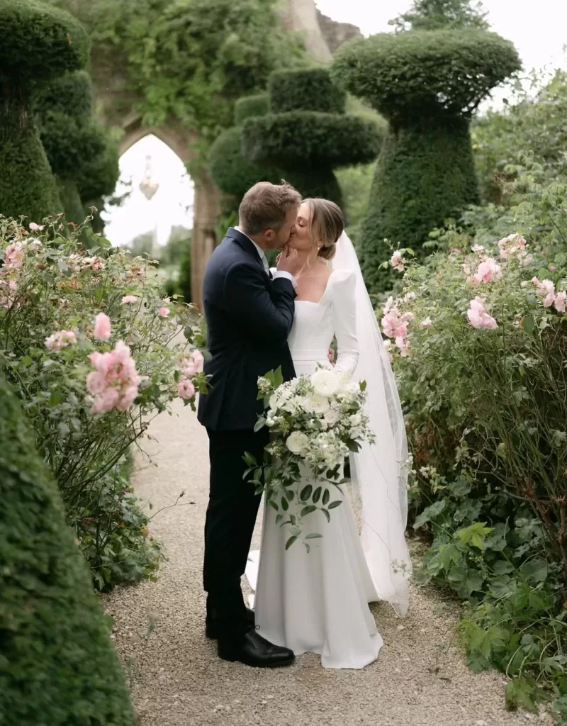 The couple shares an intimate moment in the gardens of Euridge Manor, with lush greenery as their backdrop.