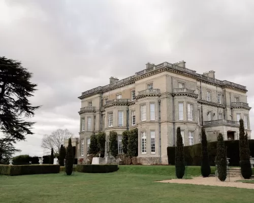 Majestic manor house framed by manicured gardens and dramatic skies, photographed by Sharon Cudworth.