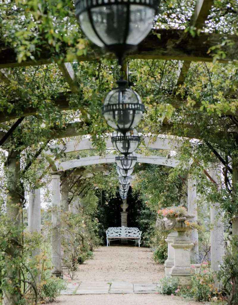A romantic garden pergola at Euridge Manor with vintage hanging lanterns and a bench at the end of the path.