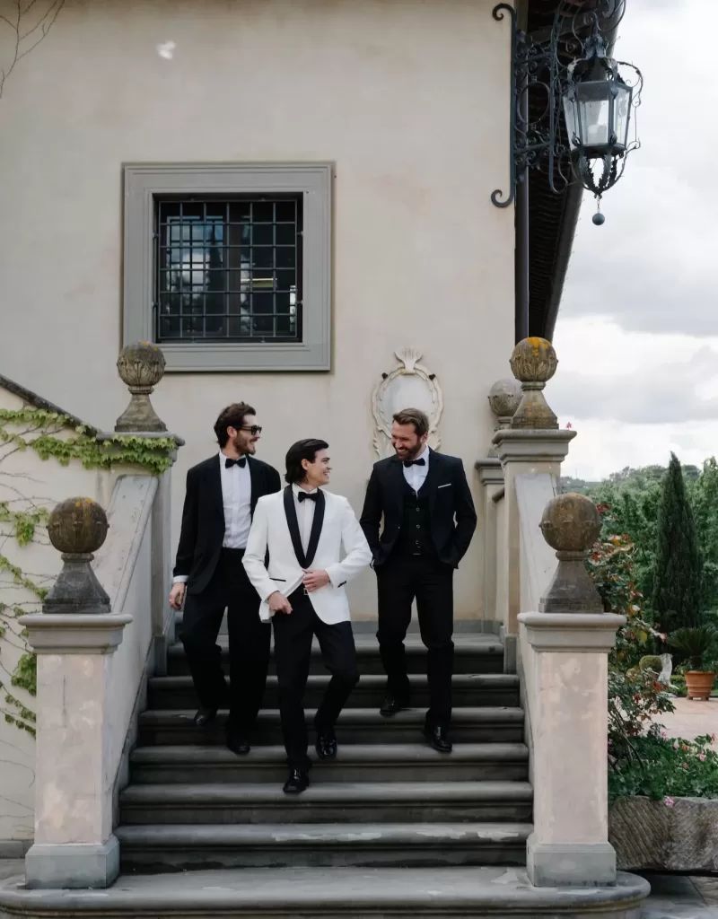 Groom and groomsmen in classic tuxedos sharing a lighthearted moment on the villa steps at Tenuta Corbinaia.